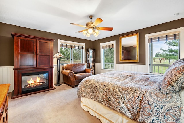 bedroom with light colored carpet, a wainscoted wall, access to exterior, and a glass covered fireplace