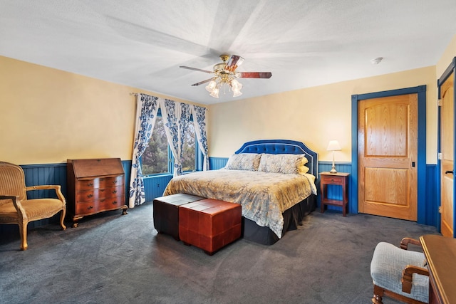 carpeted bedroom with wainscoting and ceiling fan