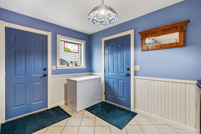 entrance foyer with light tile patterned floors and a wainscoted wall