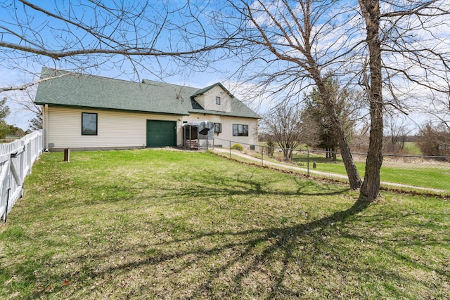 back of property with a shingled roof, a garage, a lawn, and a fenced backyard