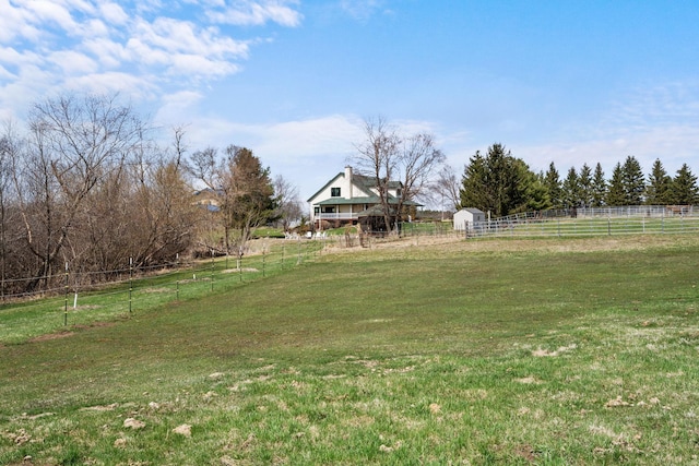 view of yard featuring a rural view, an outdoor structure, and fence