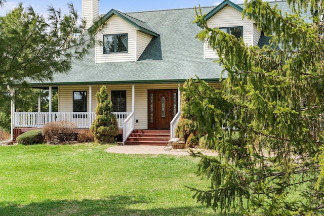 new england style home featuring a chimney, a front yard, roof with shingles, and covered porch