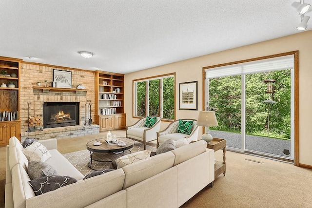 living room featuring built in shelves, carpet, visible vents, a brick fireplace, and a textured ceiling