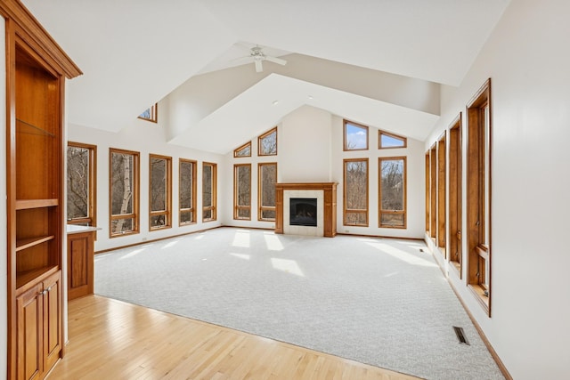 unfurnished living room with high vaulted ceiling, a ceiling fan, a tile fireplace, light wood-style flooring, and visible vents