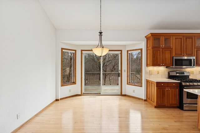 kitchen with decorative backsplash, light wood-type flooring, stainless steel appliances, light countertops, and baseboards