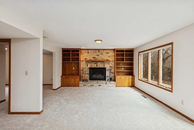 unfurnished living room with carpet, visible vents, baseboards, a brick fireplace, and built in shelves