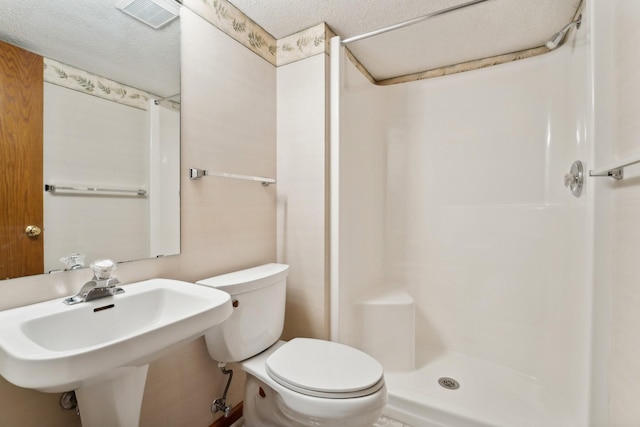 full bathroom with a shower stall, a sink, a textured ceiling, toilet, and visible vents