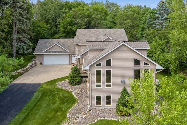 view of front facade featuring a garage, driveway, a shingled roof, and a wooded view