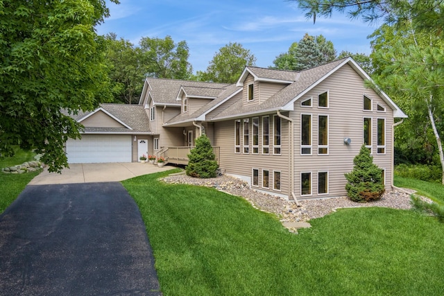 view of front of house featuring an attached garage, driveway, roof with shingles, and a front yard