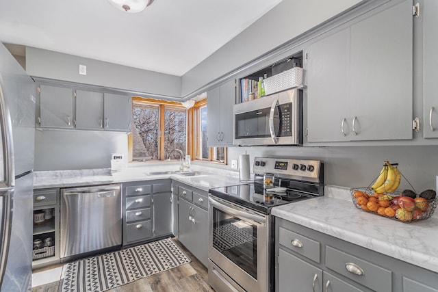 kitchen featuring a sink, appliances with stainless steel finishes, wood finished floors, and gray cabinets