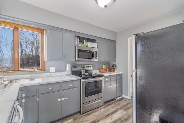 kitchen featuring open shelves, gray cabinets, light countertops, appliances with stainless steel finishes, and wood finished floors