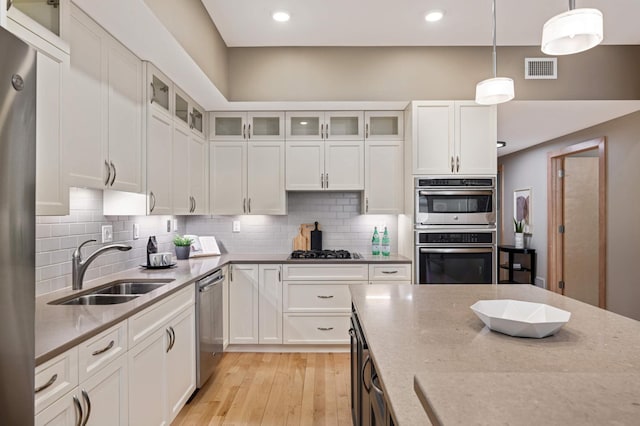 kitchen with stainless steel appliances, tasteful backsplash, light wood-style flooring, white cabinetry, and a sink