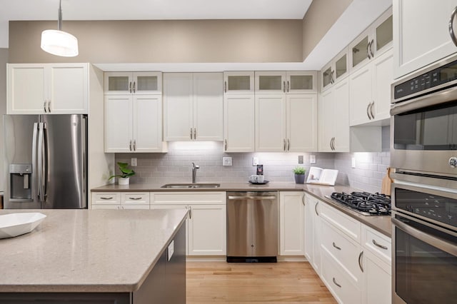 kitchen with stainless steel appliances, light wood-type flooring, a sink, and tasteful backsplash