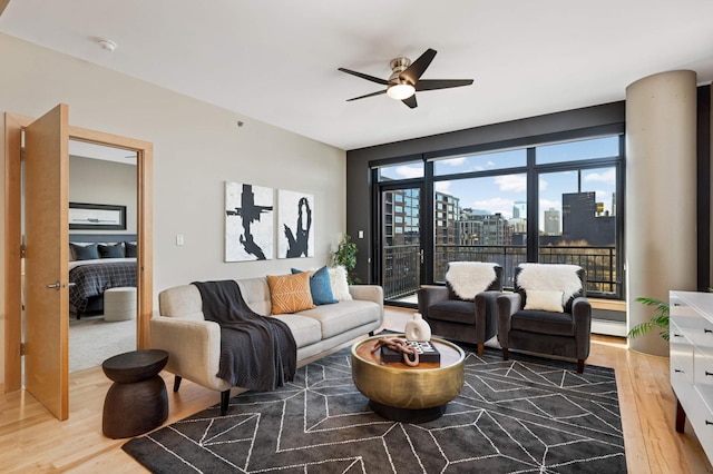 living area featuring a view of city, ceiling fan, a baseboard heating unit, and wood finished floors