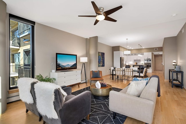 living area featuring light wood-style floors, a baseboard radiator, floor to ceiling windows, and ceiling fan