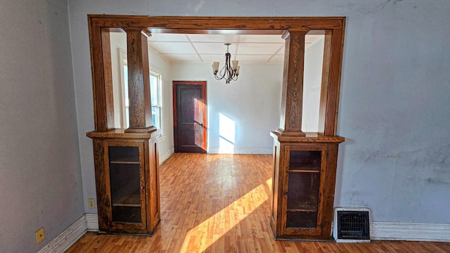 hall featuring a drop ceiling, wood finished floors, baseboards, and ornate columns