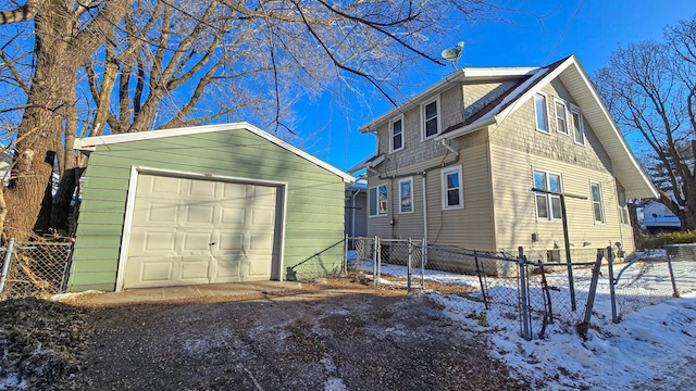 view of snowy exterior featuring an outbuilding, a detached garage, and fence