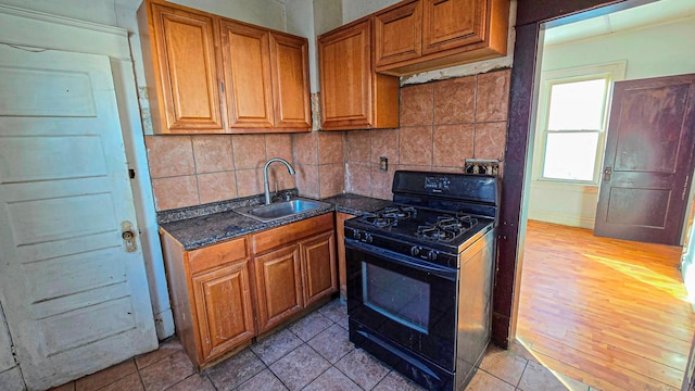 kitchen with light wood finished floors, brown cabinetry, decorative backsplash, black range with gas cooktop, and a sink