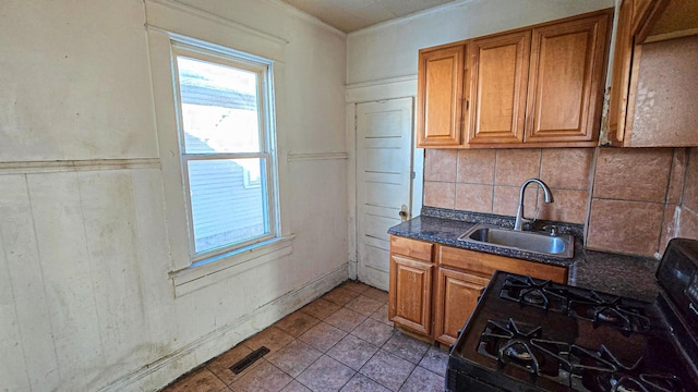 kitchen featuring black gas stove, brown cabinetry, visible vents, and a sink