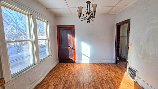 unfurnished dining area with a notable chandelier, wood finished floors, visible vents, and baseboards