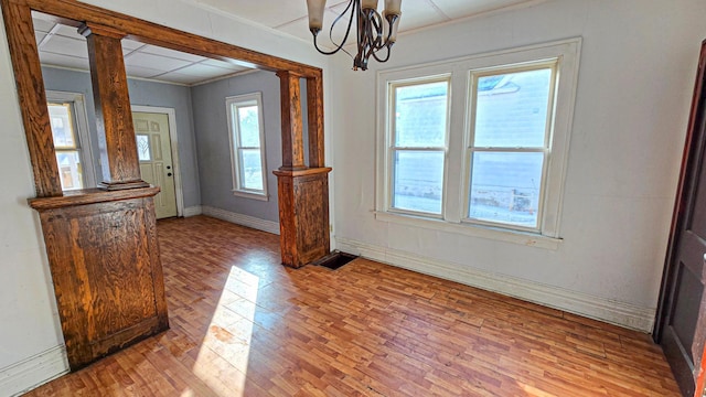 unfurnished dining area featuring crown molding, light wood-style flooring, decorative columns, and baseboards