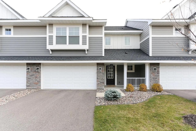 view of property with aphalt driveway, an attached garage, stone siding, roof with shingles, and board and batten siding