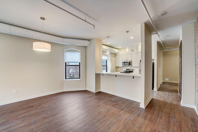 kitchen featuring dark wood finished floors, a breakfast bar, stainless steel appliances, light countertops, and decorative light fixtures