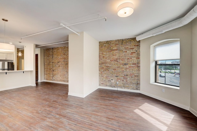 unfurnished room with wood finished floors, baseboards, and brick wall