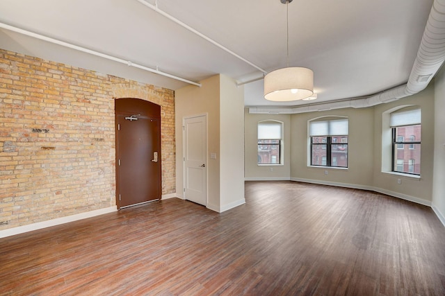 empty room with wood finished floors, baseboards, brick wall, and arched walkways