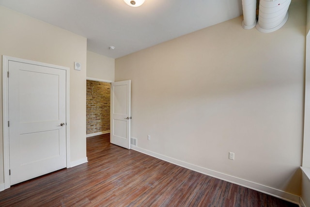 unfurnished bedroom featuring wood finished floors, baseboards, and brick wall