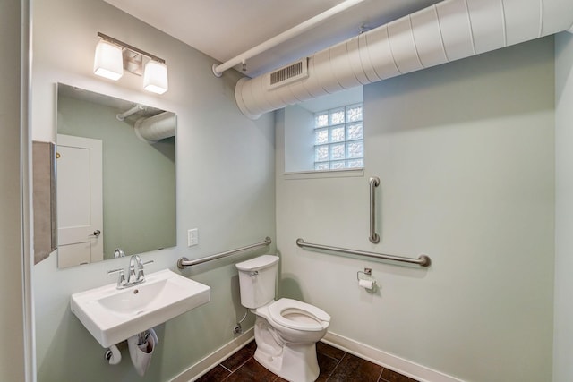 half bath with visible vents, toilet, baseboards, and a sink