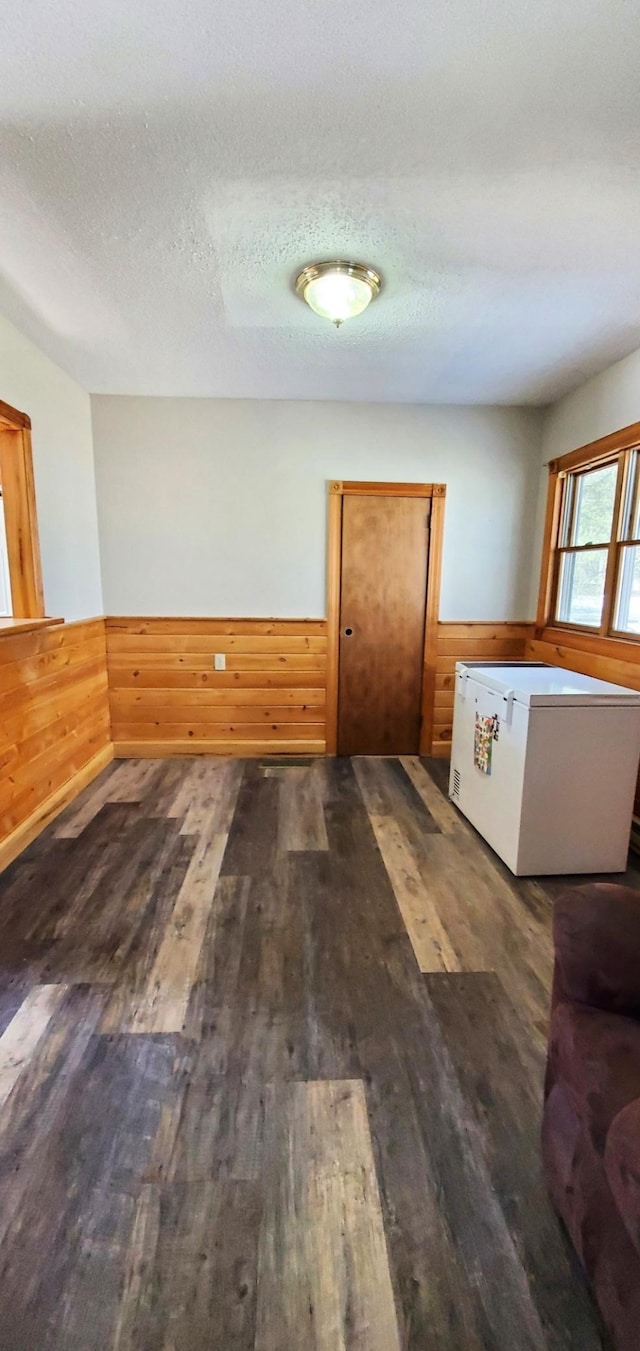 interior space featuring wooden walls, wood finished floors, a textured ceiling, and wainscoting