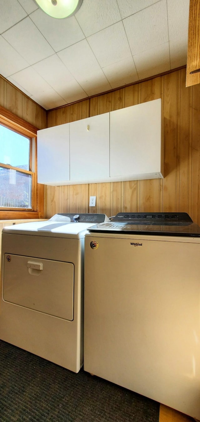 laundry room featuring wooden walls, cabinet space, and washer and dryer