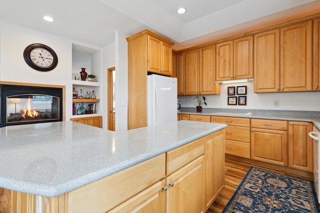 kitchen with recessed lighting, light stone countertops, freestanding refrigerator, wood finished floors, and a multi sided fireplace