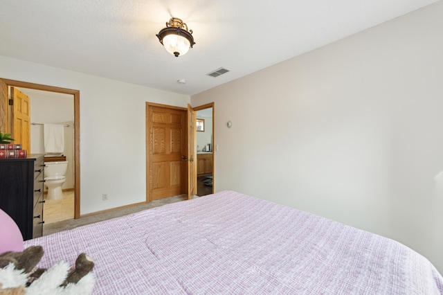 bedroom with light colored carpet, visible vents, ensuite bath, and baseboards