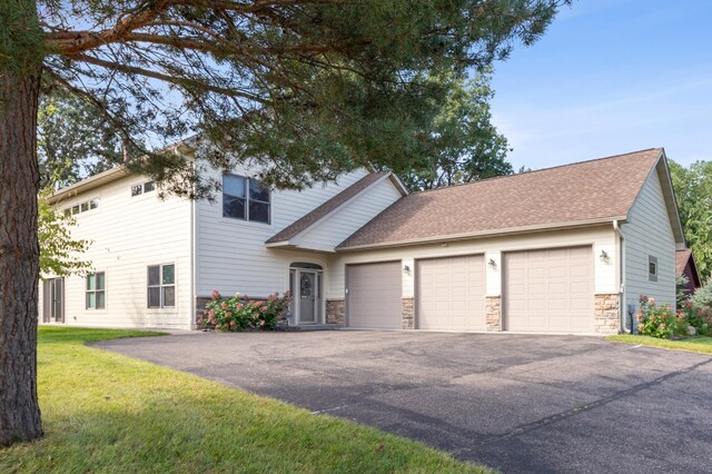 view of front of house with an attached garage, stone siding, driveway, roof with shingles, and a front yard