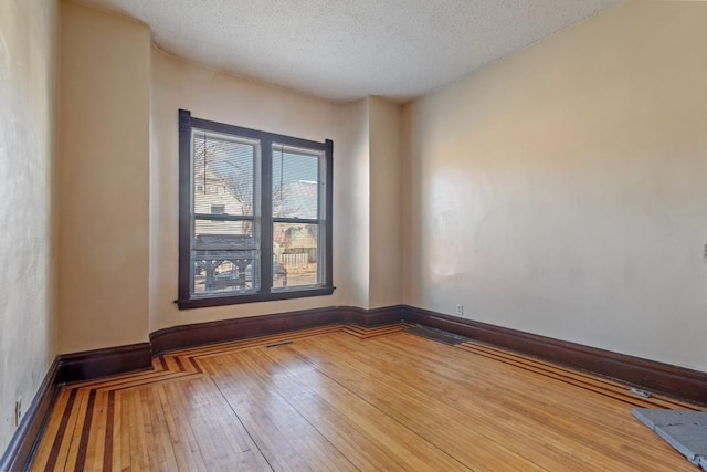 spare room with a textured ceiling, hardwood / wood-style floors, and baseboards