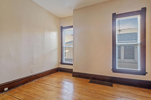 empty room with light wood-style flooring, visible vents, and baseboards