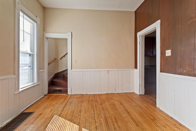 unfurnished room with a healthy amount of sunlight, visible vents, hardwood / wood-style floors, and stairs