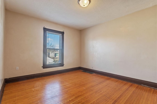 unfurnished room featuring wood-type flooring, visible vents, a textured ceiling, and baseboards