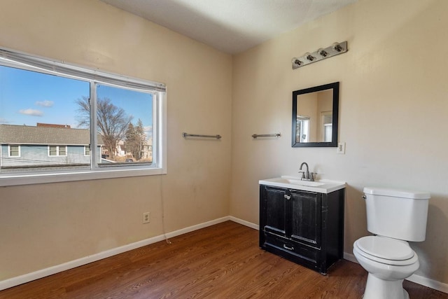 half bath with vanity, wood finished floors, toilet, and baseboards