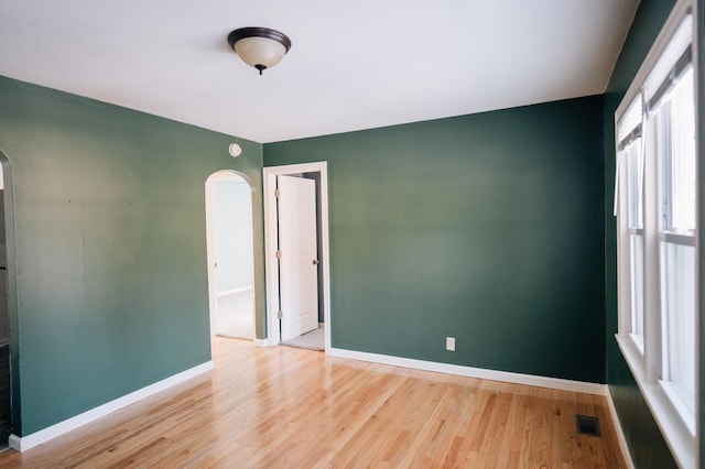 unfurnished room with wood finished floors, visible vents, arched walkways, and baseboards