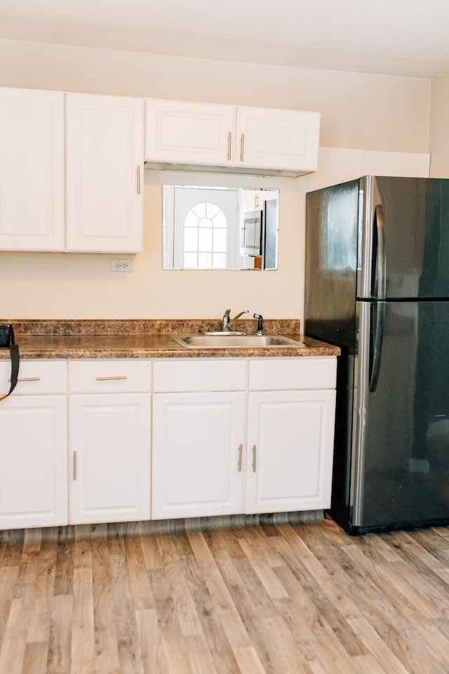 kitchen featuring light wood finished floors, white cabinets, freestanding refrigerator, and a sink