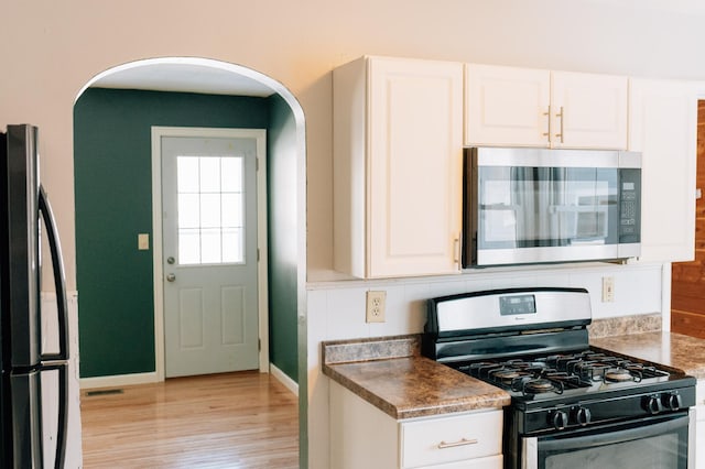 kitchen featuring stainless steel appliances, arched walkways, light wood-style floors, and white cabinets