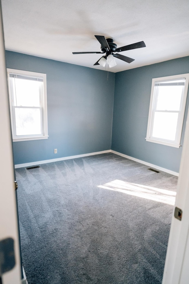 carpeted empty room with visible vents, baseboards, and a ceiling fan