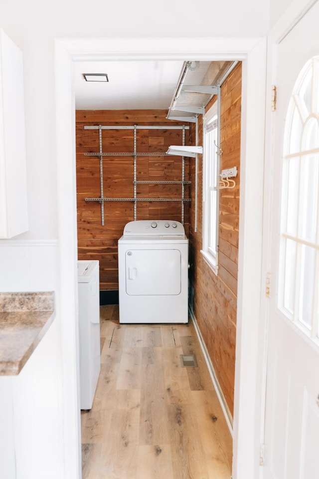 washroom featuring light wood finished floors, laundry area, wood walls, and separate washer and dryer