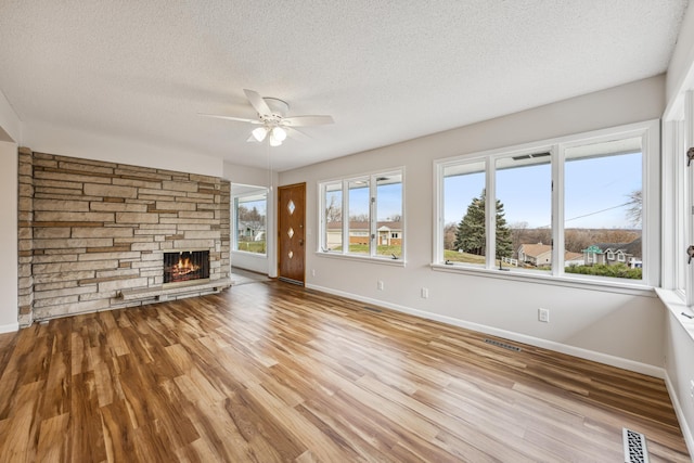 unfurnished living room featuring a textured ceiling, a stone fireplace, wood finished floors, visible vents, and baseboards