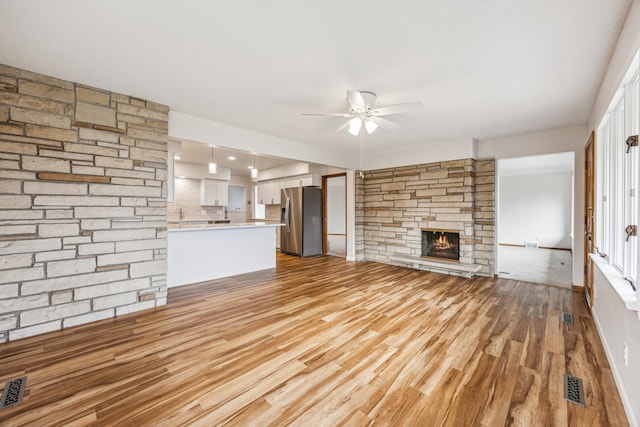 unfurnished living room with ceiling fan, light wood finished floors, a fireplace, and visible vents