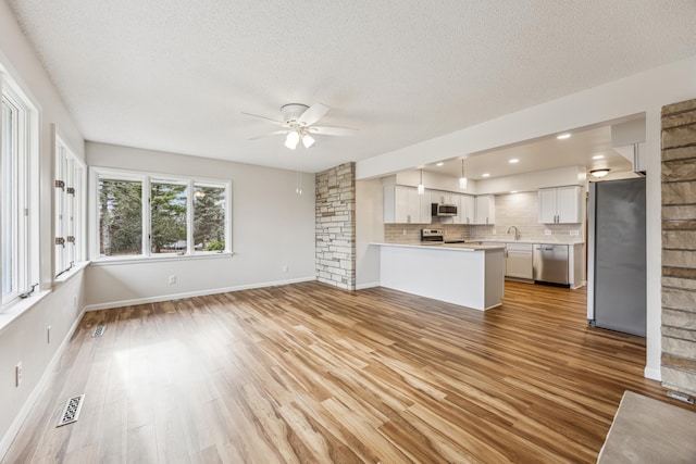 unfurnished living room with ceiling fan, baseboards, visible vents, and light wood-style floors