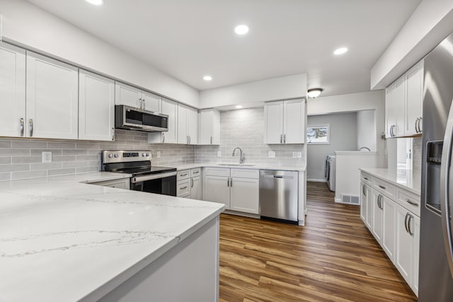 kitchen featuring tasteful backsplash, appliances with stainless steel finishes, dark wood-type flooring, light stone countertops, and a sink